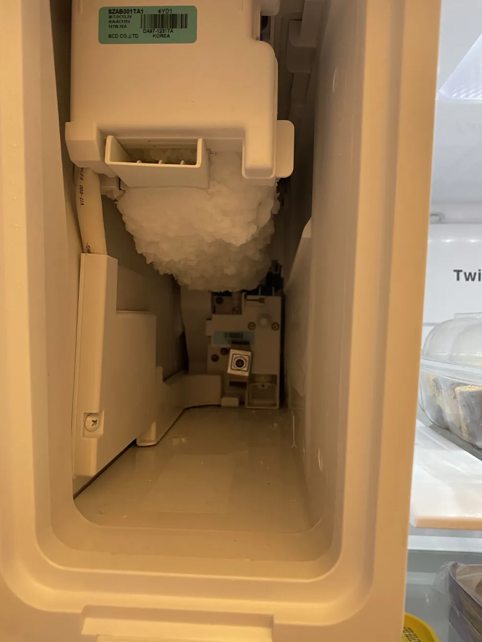 Samsung DA97-12317A ice maker frozen over inside the ice compartment of a French-door refrigerator on a Minneapolis, MN service call — large ball of ice surrounding the fill tube and module, exposed control board visible behind.